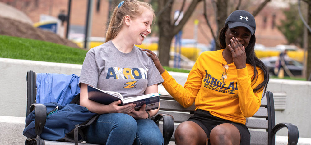 Two students share a laugh on a bench on the Akron campus