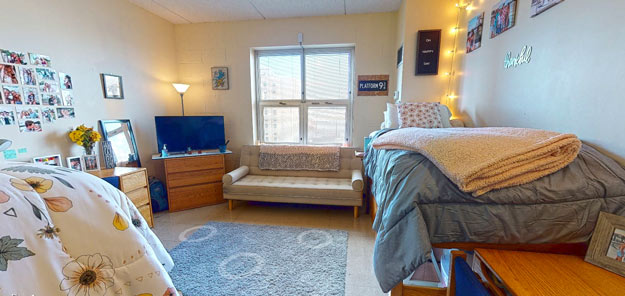 A bright residence hall room with a couch, desk, tv and bed.