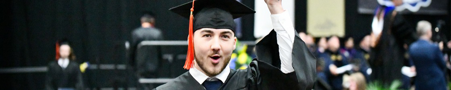 male graduate from The University of Akron holding diploma above head