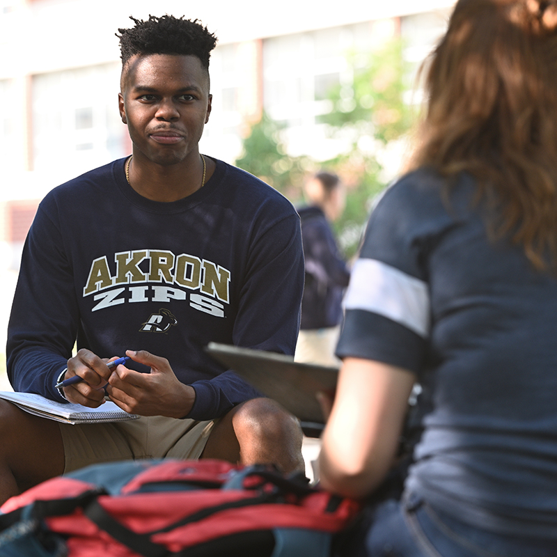 Three students share a laugh while seated outdoors on the UA campus