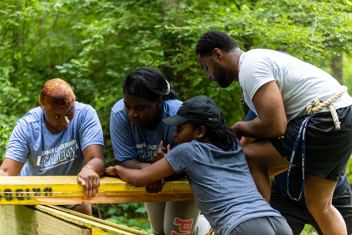 Four CoB Summer Leadership Academy students leaning on a wood beam