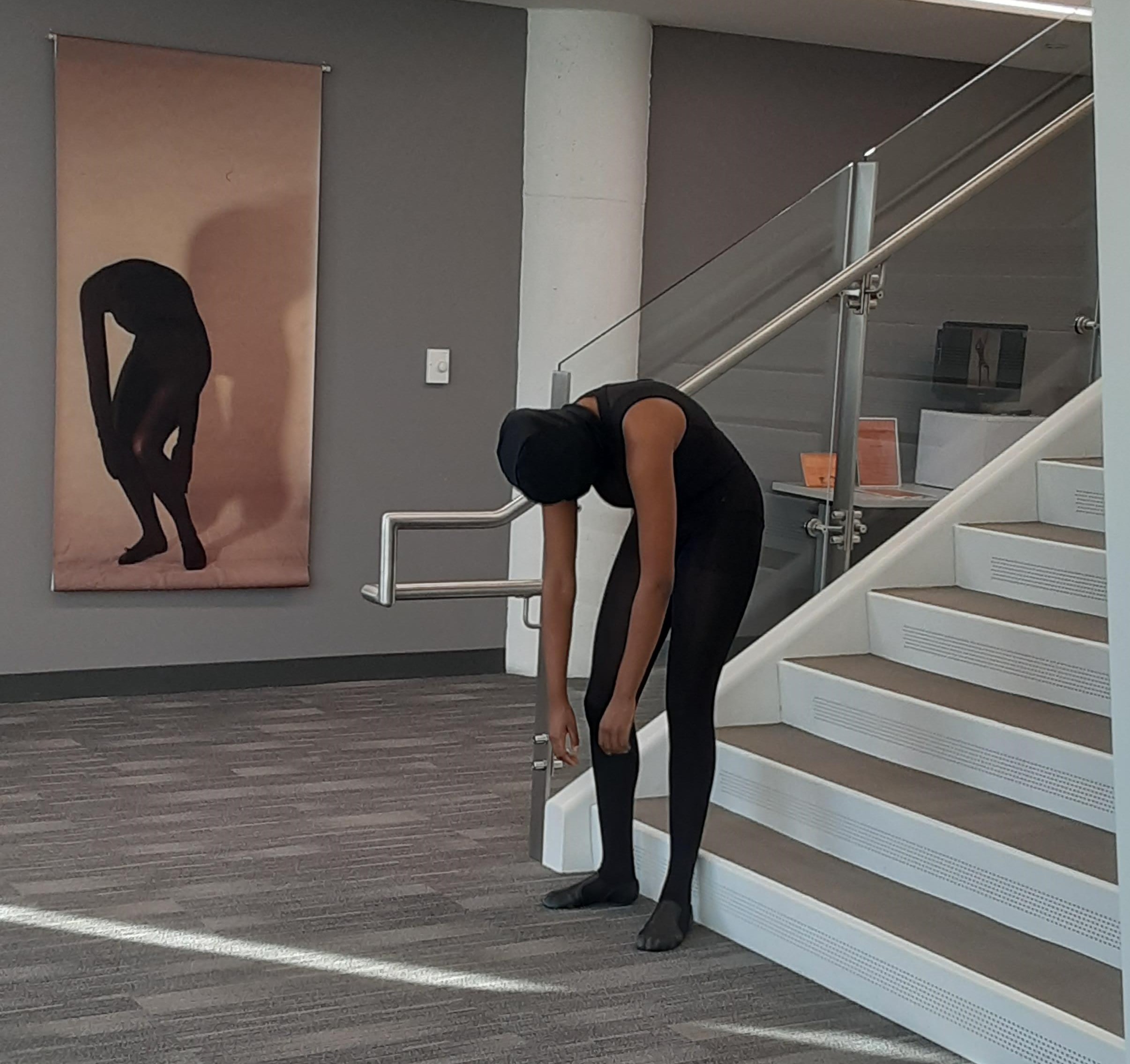 man in all black posed facing downward. in the background, a man in a photo does the same