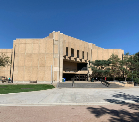 Bierce Library, a tan concrete building, on a clear, blue sky day with two students walking up to the building.