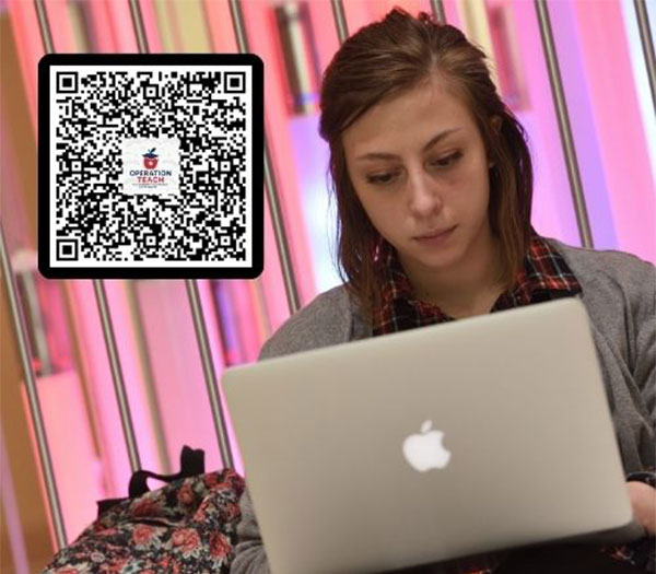 Student works on a laptop beside an Operation Teach QR code.