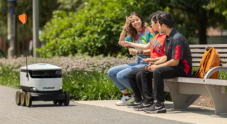 Students sitting on bench looking at food robot