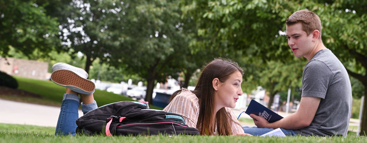 Two students discuss an English degree assignment outdoors between classes.