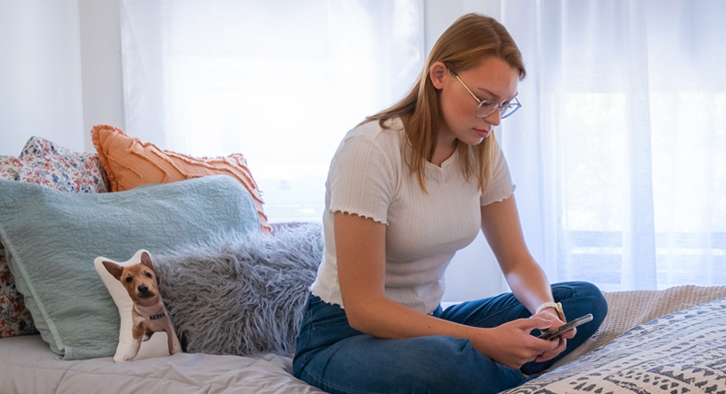 Student sitting on bed looking at mobile phone