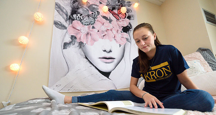 A student sitting in bed studies for an exam. Wall decorations and lights are behind her.