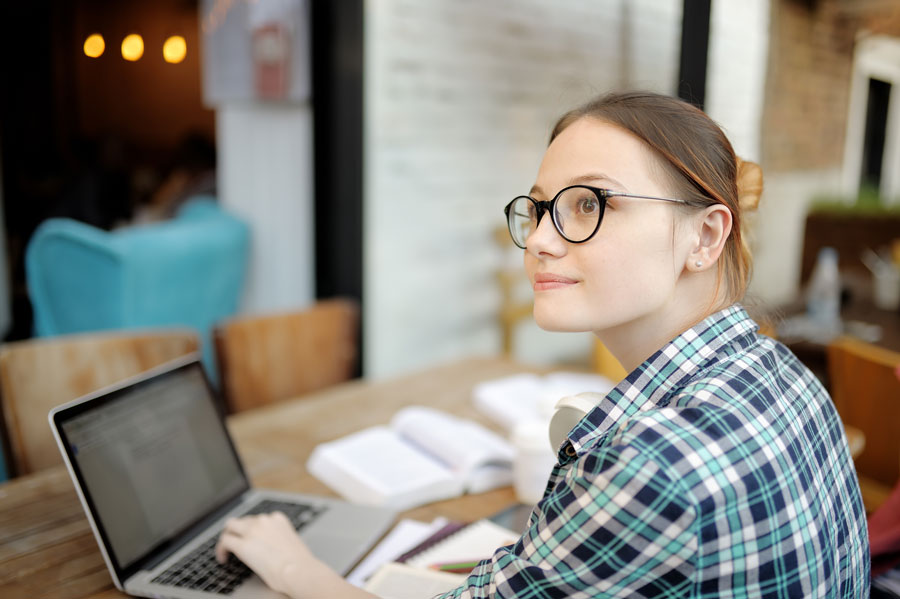 A female student sitting at a table with a laptop, looking to her side.
