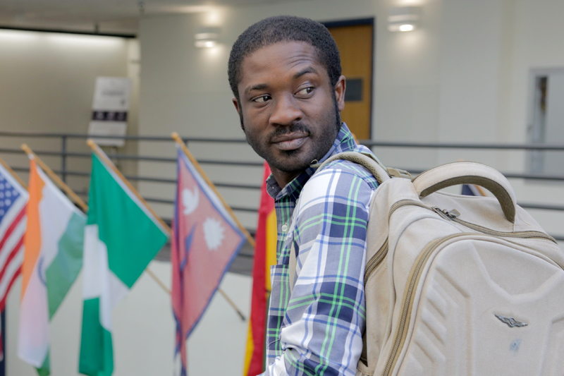 Student with a backpack looking at camera in front flags of the world.