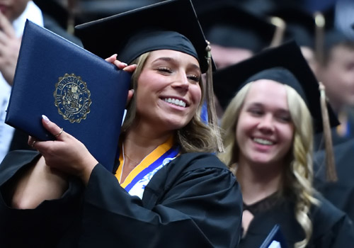 Female graduate holds up UA Diploma